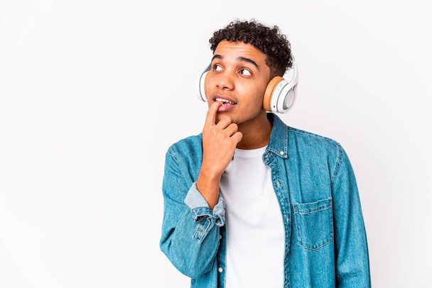 Junger afrikanisch-amerikanischer Lockenkopf isoliert Musik hörend mit Kopfhörern entspannt über etwas nachdenkend, das einen Kopierraum betrachtet. - Foto, Bild