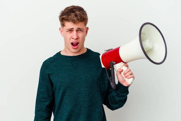 Young caucasian man holding a megaphone isolated on white background screaming very angry and aggressive. - Photo, Image
