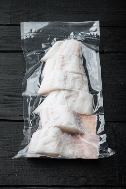 Сырая рыба пикша безкожей пластиковый вакуум упакован, на черном деревянном столе - Фото, изображение