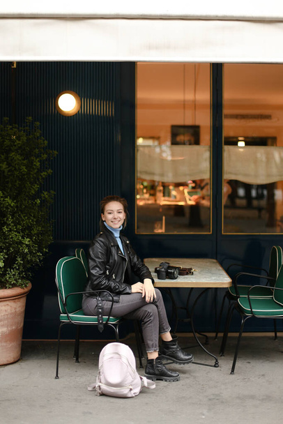 Nuori hymyilevä nainen istuu katukahvilassa kameran kanssa. - Valokuva, kuva