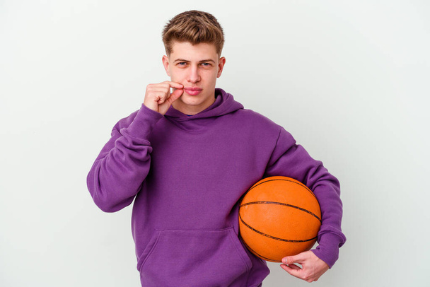 Giovane uomo caucasico che gioca a basket isolato sfondo con le dita sulle labbra mantenendo un segreto. - Foto, immagini