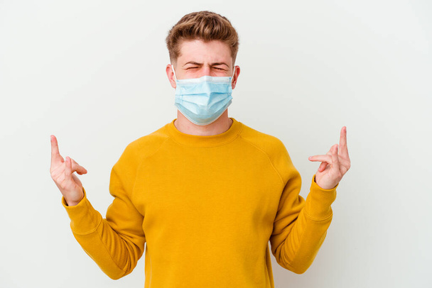 Young man wearing a mask for coronavirus isolated on white background showing rock gesture with fingers - Photo, Image