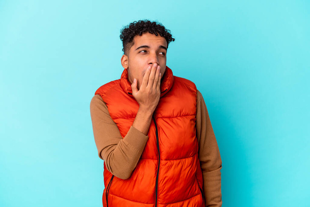 Young african american curly man isolated on blue yawning showing a tired gesture covering mouth with hand. - Photo, image