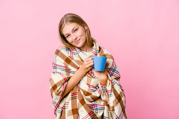 Jeune femme russe enveloppée dans une couverture boire du café a une expression amicale, pressant la paume à la poitrine. Concept d'amour. - Photo, image
