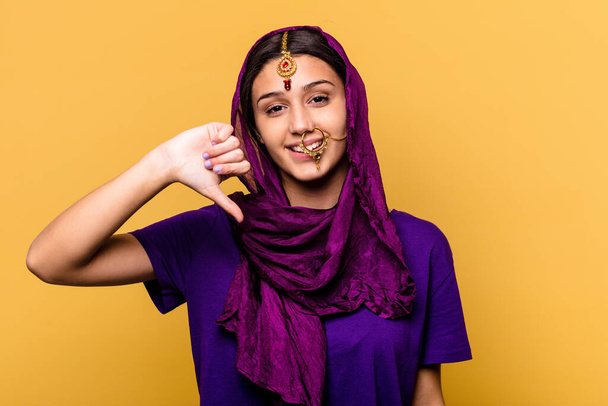 Νεαρή Ινδή που φοράει παραδοσιακά ρούχα σάρι απομονωμένα σε κίτρινο φόντο δείχνοντας μια χειρονομία αντιπάθειας, με τους αντίχειρες κατεβασμένους. Έννοια διαφωνίας. - Φωτογραφία, εικόνα