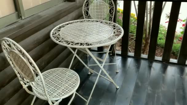 Dvě bílé kovové židle a malý kulatý stolek na hnědé dřevěné terase. Série nábytku. 4K - Záběry, video