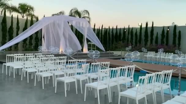 Tradições judaicas casamento cerimônia ao ar livre. Casamento dossel (chuppah, hupa) feito de tecido branco contra o fundo do céu da noite, palmas e um reservatório artificial decorado com balões. HD - Filmagem, Vídeo