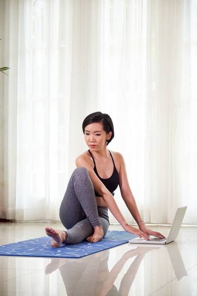 Ajuste a jovem mulher asiática fazendo torção espinhal sentada para se exercitar ao trabalhar no laptop - Foto, Imagem