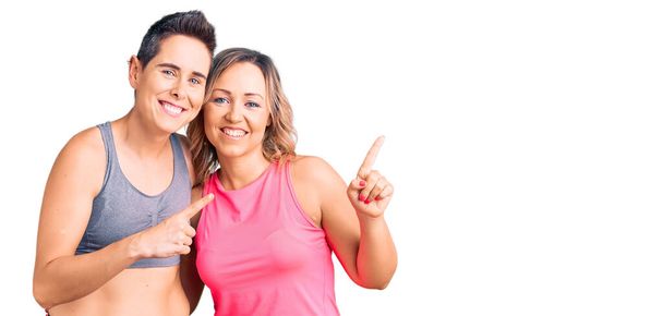 スポーツウェアを身に着けている女性のカップル笑顔とカメラを見て2本の手と指で側面を指して.  - 写真・画像