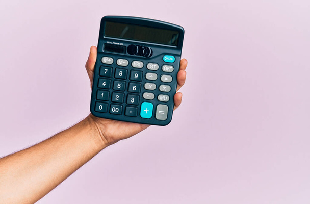 Hand of young hispanic man holding calculator over isolated pink background. - Foto, Imagem