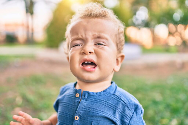 Cute and sad little boy crying having a tantrum at the park on a sunny day. Beautiful blonde hair male toddler frustrated with tears on face outdoors - Fotoğraf, Görsel