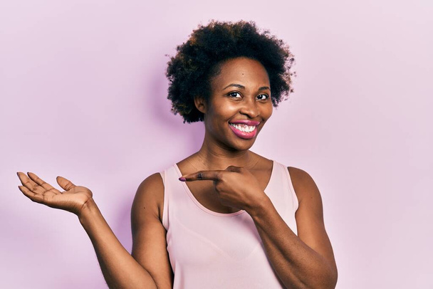 Mladá afro americká žena na sobě ležérní tričko bez rukávů ohromený a usmívá se do kamery při prezentaci s rukou a ukazuje prstem.  - Fotografie, Obrázek