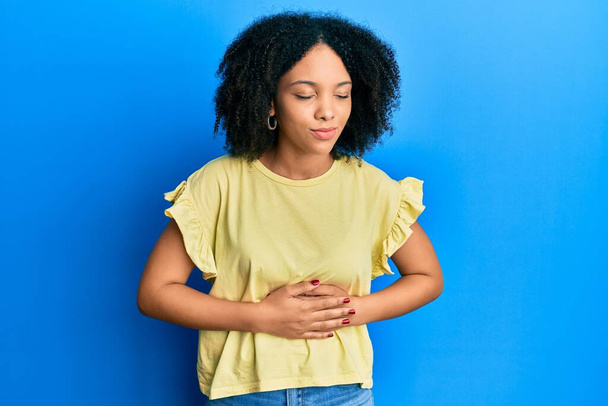 Jong Afrikaans-Amerikaans meisje draagt casual kleding met de hand op de maag omdat indigestie, pijnlijke ziekte zich onwel voelt. pijnconcept.  - Foto, afbeelding
