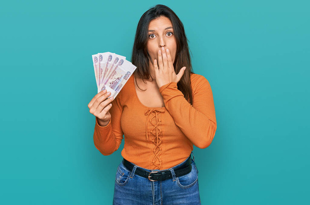 Mooie Spaanse vrouw met Russische 500 roebel bankbiljetten die mond met hand bedekken, geschokt en bang voor fouten. verraste uitdrukking  - Foto, afbeelding