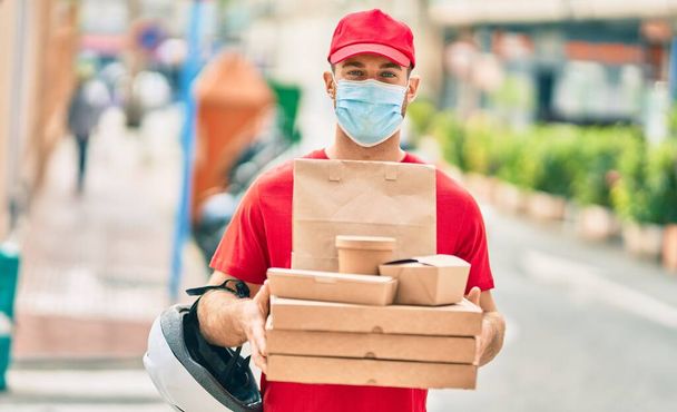 Young caucasian deliveryman wearing medical mask  holding delivery food at the city. - Foto, Imagem