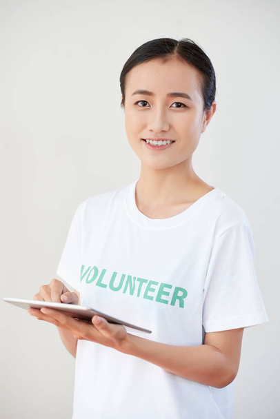 Glücklich lächelndes junges Mitglied der Freiwilligenorganisation füllt Dokument oder Fragebogen auf Tablet-Computer aus - Foto, Bild