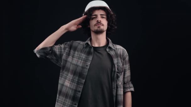 Un ingénieur joyeux porte un casque spécial sur la tête, vêtu d'une chemise à carreaux, sur un fond noir, en studio, - Séquence, vidéo