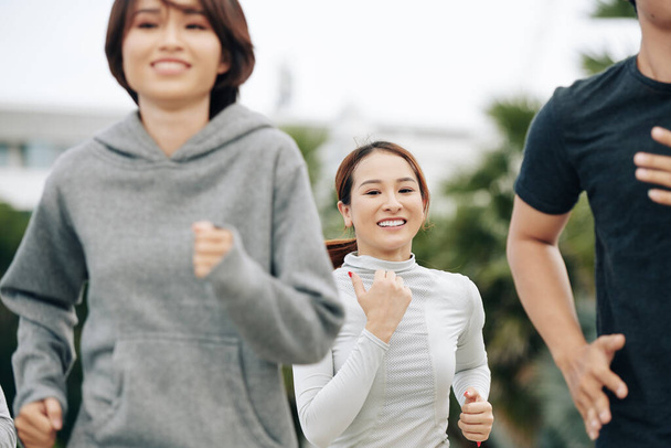 Schöne junge, fitte Frau lächelt in die Kamera, wenn sie mit ihren Freunden im Freien joggt - Foto, Bild