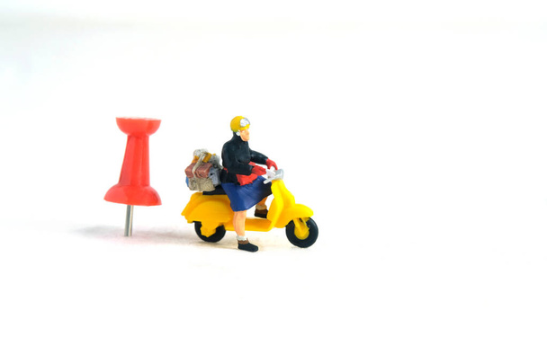 Miniature people toys conceptual photography. Courier pinpoint location pickup package delivery service. Postman with red push pin, isolated white background. - Photo, Image