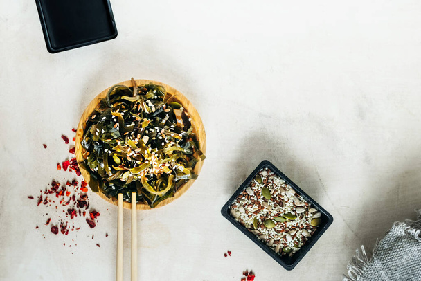 hínár ébredés saláta szezámmaggal kerek bambusz tányéron, bambusz pálcika, magvak szóráshoz. otthon főzés egészséges vegán öko ételeket. egyszerű ázsiai receptek otthon. hínártányérok. szelektív fókusz - Fotó, kép