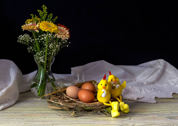 La composición de Pascua. Huevos, juguetes un ramo de gerberas coloridas y velas de iglesia en la mesa de madera de cerca. - Foto, Imagen