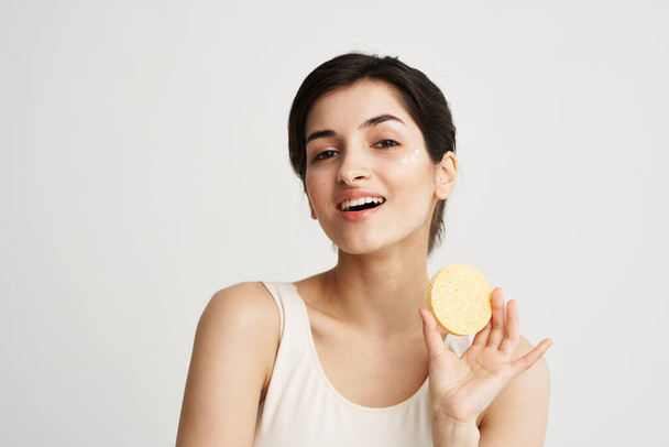 Mujer bonita alegre con una esponja en las manos cuidado de la piel cosméticos color fondo claro - Foto, imagen