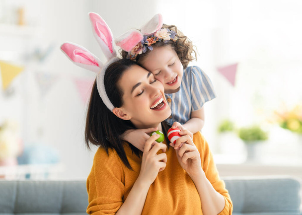 Happy holiday! Mother and her daughter with painting eggs. Family celebrating Easter. Cute little child girl is wearing bunny ears.  - Foto, Imagem