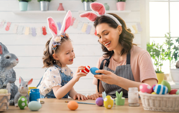 Matka i jej córka malują jajka. Szczęśliwa rodzina przygotowuje się do Wielkanocy. słodkie małe dziecko dziewczyna noszenie królicze uszy. - Zdjęcie, obraz