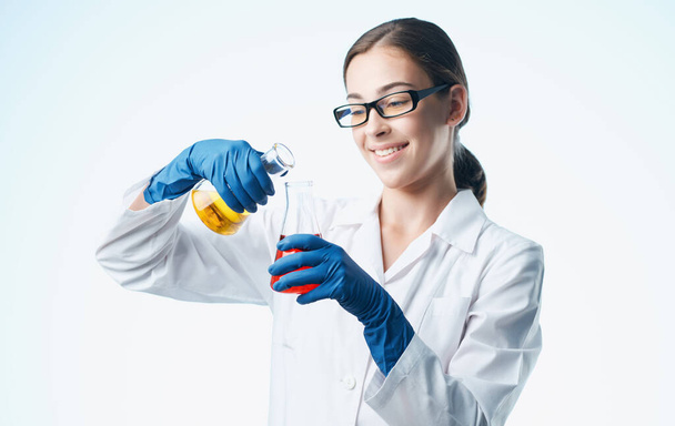 une infirmière en blouse de laboratoire et des gants bleus avec une fiole dans sa main analyses de laboratoire d'éléments chimiques - Photo, image
