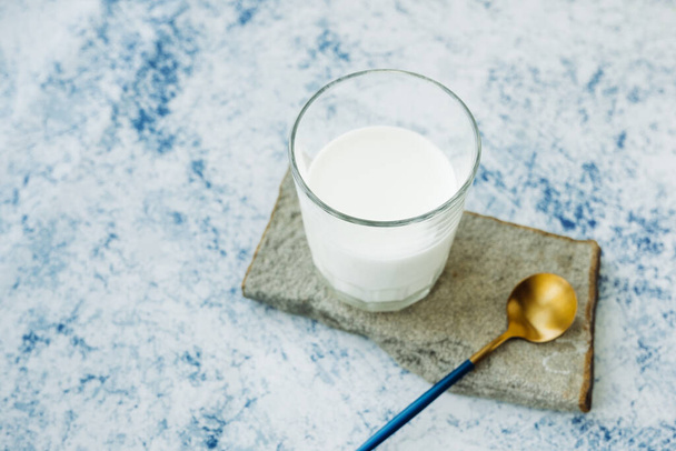 чашка молока на подставке из натурального камня и стильная золотая ложка. минимализм в еде. блог или сайт о продуктах питания - Фото, изображение