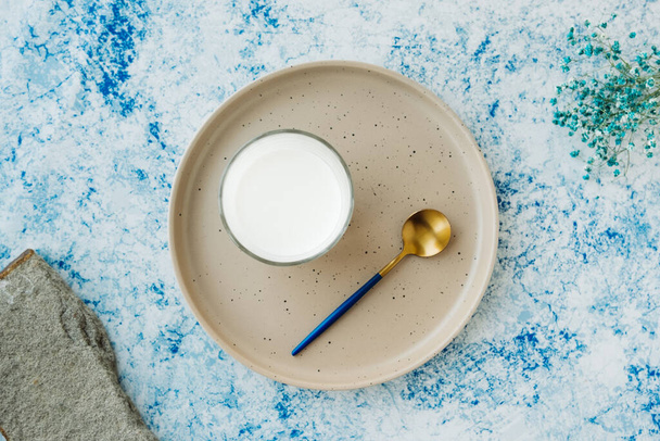 kopje melk en stijlvolle gouden lepel versierd met natuurlijke materialen: echte steen en gedroogde blauwe bloemen. minimalisme in voedsel. blog of website over voedselinhoud - Foto, afbeelding
