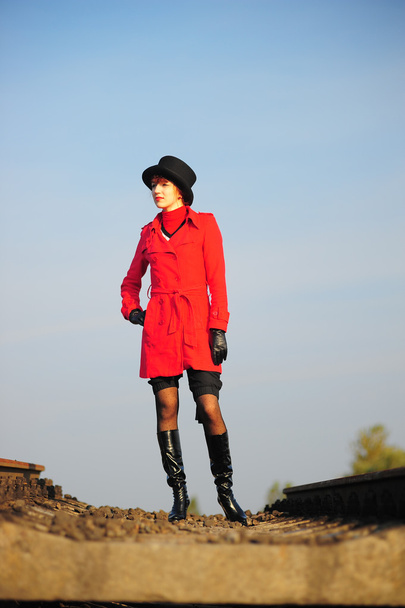 The young red-haired woman going on railroad tracks in brightly red jacket - Foto, afbeelding