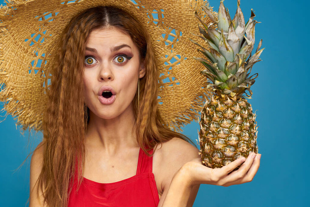 Una donna con un cappello di paglia con un ananas tra le mani o è un divertente sfondo di frutta esotica blu - Foto, immagini