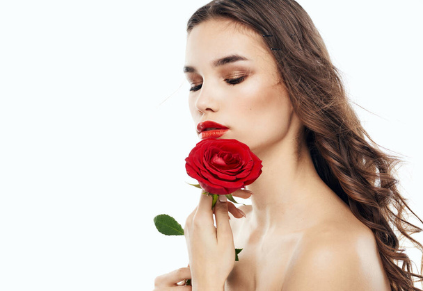 Charming brunette woman with bare shoulders and a fragrant flower near her face - Фото, зображення
