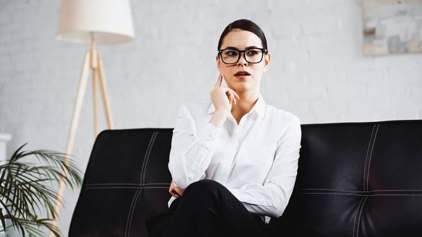 thoughtful businesswoman looking away while sitting on couch in office - Photo, Image