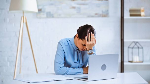 mujer de negocios agotada sentada cerca de la computadora portátil con la cabeza inclinada - Foto, Imagen