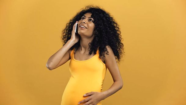 妊娠中のパニック女性は笑顔と黄色に隔離されたスマートフォンで話す - 写真・画像