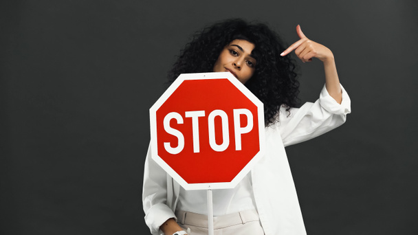 hispanic woman pointing at signboard with stop lettering isolated on black  - Photo, Image