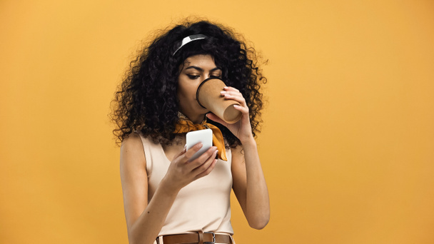 hispanic woman with coffee to go and smartphone isolated on yellow - Photo, Image