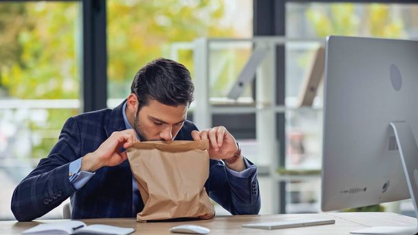 Geschäftsmann riecht Papiertüte mit Essen zum Mitnehmen im Büro - Foto, Bild