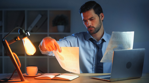 hombre de negocios mirando documentos mientras trabaja hasta tarde en la oficina - Foto, Imagen