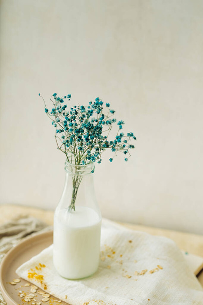 Cyganka niebieska w szklanej przezroczystej butelce z białą wodą lub mlekiem. prosty naturalny wystrój domu. Beżowy monochromatyczny. ukierunkowanie selektywne - Zdjęcie, obraz