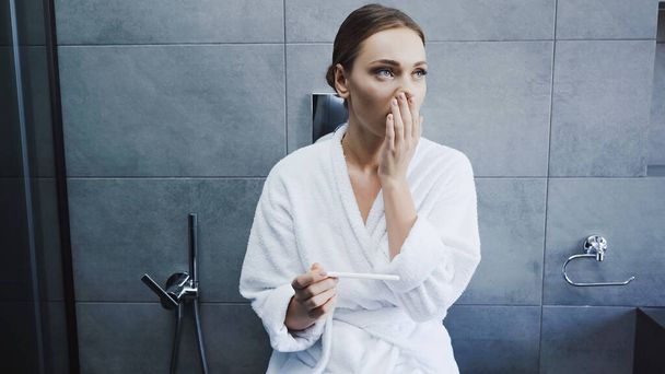 surpris jeune femme en peignoir tenant test de grossesse dans la salle de bain - Photo, image