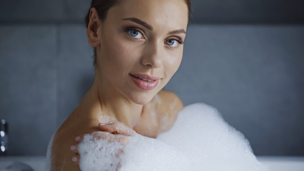 jeune femme prenant un bain avec de la mousse et regardant la caméra - Photo, image