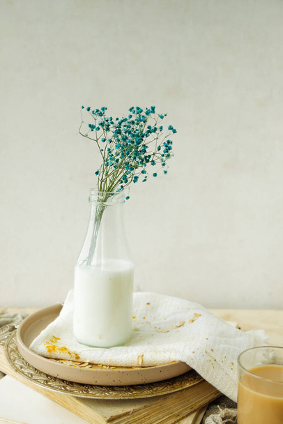 gypsophila azul en botella de vidrio transparente con agua blanca o leche. decoración casera natural simple. Monocromo beige. enfoque selectivo - Foto, imagen