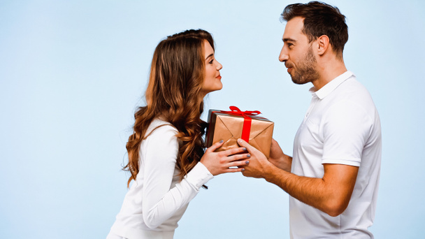 side view of boyfriend giving wrapped present to girlfriend isolated on blue - Photo, Image