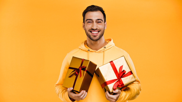 hombre alegre sosteniendo regalos envueltos aislados en amarillo - Foto, imagen