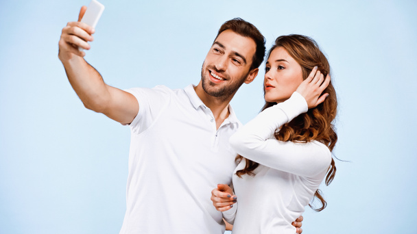 νεαρό ζευγάρι που βγάζει selfie απομονωμένο στο μπλε - Φωτογραφία, εικόνα
