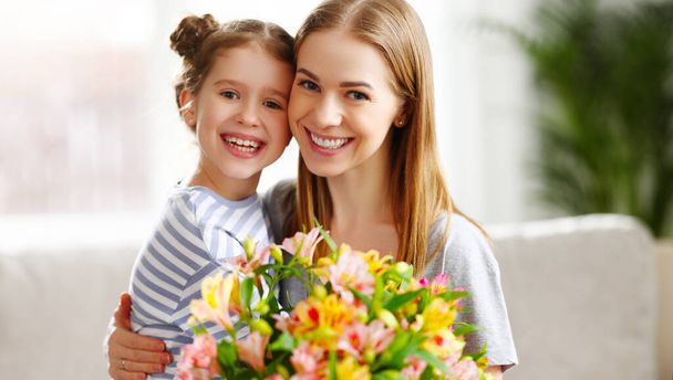 Cheerful kid embracing woman sitting on sofa with bouquet of Alstroemeria flowers on Mothers Day - Foto, immagini
