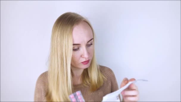 A fehér hátterű lány elolvassa a gyógyszerekre vonatkozó utasításokat. A nő megnézi a gyógyszer listáját és összetételét. Az otthoni öngyógyászat fogalma és a kábítószerek tulajdonságainak tanulmányozása - Felvétel, videó